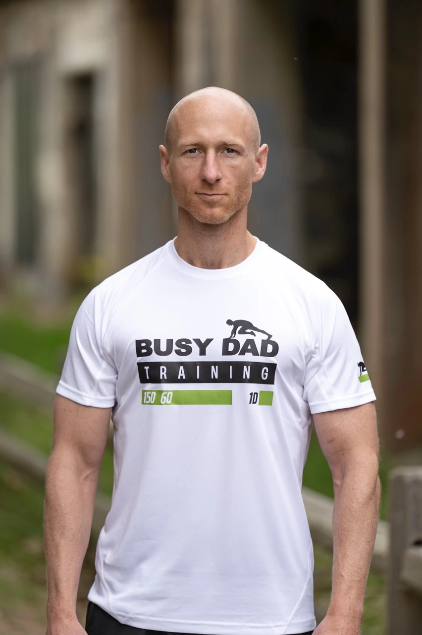 Busy dad training coach demonstrating bodyweight squat form during a home workout